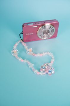 a pink camera sitting on top of a blue table next to a beaded necklace