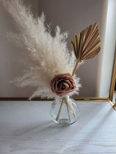 a vase filled with white feathers and a flower on top of a table next to a mirror