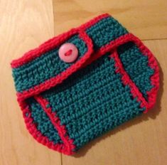 a crocheted purse with a pink button on the front and green trim around it