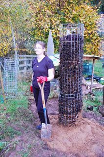 a woman standing next to a tree with a shovel in her hand and an animal cage behind her