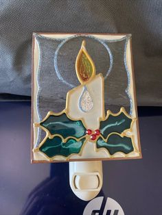 a lit candle with holly leaves and red berries on it is attached to a light switch