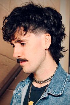 a man with a moustache wearing a blue jean jacket and a chain around his neck