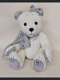 a white teddy bear with a bow on it's head and feet sitting down