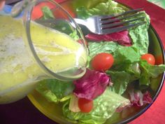 a salad with lettuce, tomatoes and dressing being poured into it on a yellow plate