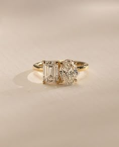 three stone engagement ring with diamond accents in yellow gold and white gold, on a plain surface