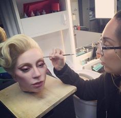 a woman is getting her makeup done by another woman in the mirror and she is wearing a fake head