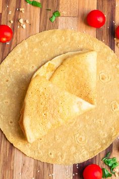 an uncooked tortilla on a cutting board with cherry tomatoes and basil