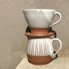 two coffee mugs stacked on top of each other in front of a stucco wall