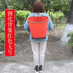 a woman holding a red basket in front of her back with trees and bushes behind her