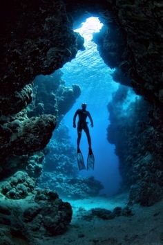 a man swimming in the ocean through a cave with his scuba gear and mask on