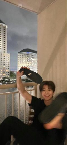 a man sitting on top of a balcony holding a skateboard in his hand and smiling at the camera