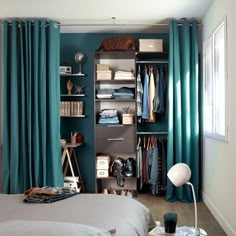 a bedroom with teal curtains and blue drapes on the windowsill, an open closet is next to a bed