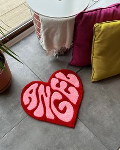 a red heart shaped rug on the floor next to a potted plant and pillow