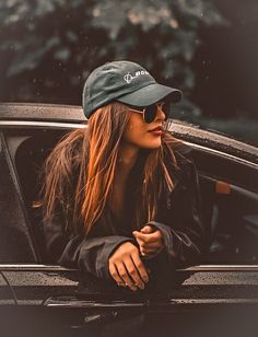 a woman in sunglasses and a hat leaning out the window of a car