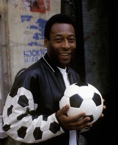 a man is holding a soccer ball in his right hand and smiling at the camera