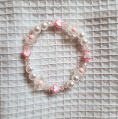 a pink and white beaded bracelet with heart charms on it's end, sitting on a bed sheet