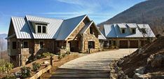 a large stone house with metal roofing on the side of a mountain road in front of mountains