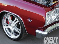 the front end of a red classic car with chrome wheels and rims on it