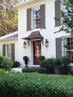 a white brick house with green shutters and two large windows on the front door