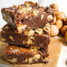 three pieces of chocolate fudge are stacked on top of each other with walnuts in the background