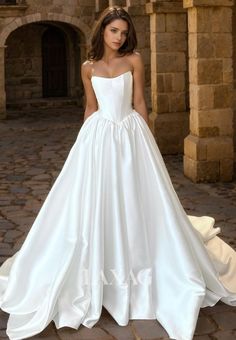 a woman wearing a white wedding dress standing in front of a stone building with her hands on her hips