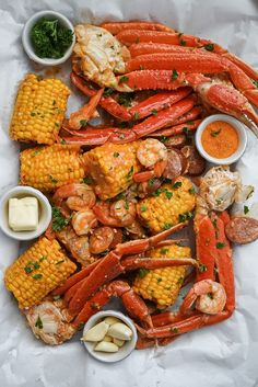 lobsters, corn on the cob and buttered potatoes are arranged in a platter