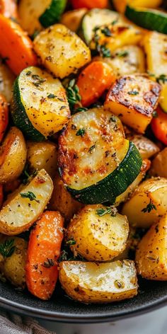 a bowl filled with potatoes, carrots and zucchini on top of a table