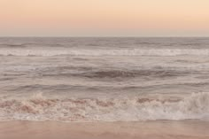 an ocean view with waves crashing on the shore and pink sky in the back ground