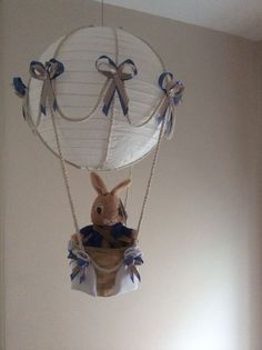 a stuffed rabbit in a basket suspended from a ceiling fixture with ribbons on the strings