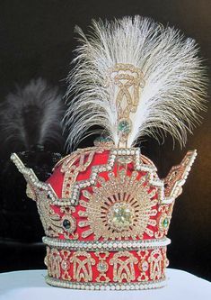 a red and white crown with feathers on it's head sitting on a table