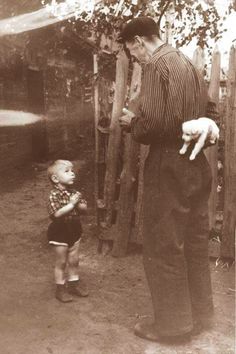 an old black and white photo of a man holding a child's hand while standing next to a fence