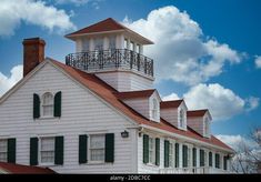 a large white house with a red roof and black shutters on the front porch