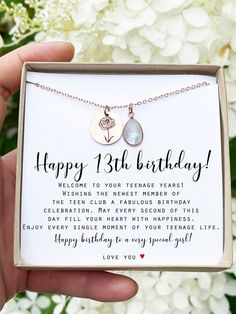 a person holding a birthday card with two hearts on it and a necklace that says happy 13th birthday