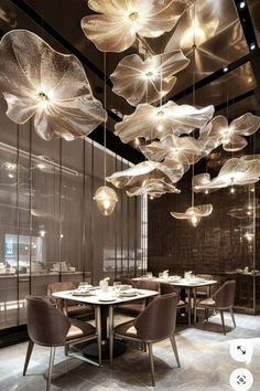 a dining room filled with lots of tables and chairs next to tall glass walls covered in hanging lights