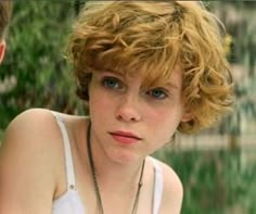 a close up of a person wearing a necklace and looking at the camera with a serious look on her face