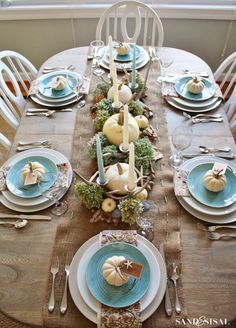 the table is set with plates, silverware and white pumpkins on top of it