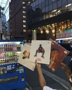 a person holding up posters in front of a vending machine on a city street