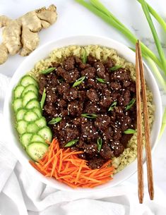 a bowl filled with meat and vegetables next to chopsticks on a white surface