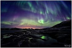 an aurora bore is seen in the sky above some ice and water at night time