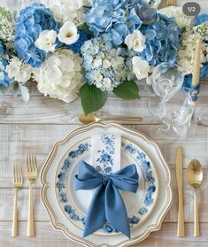 a table setting with blue and white flowers, silverware, and gold utensils