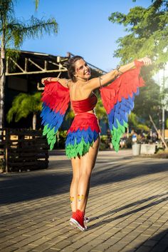 a woman in a red and blue dress is holding a colorful bird wings on her arm