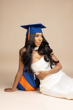 a woman sitting on the ground wearing a graduation cap and gown with long black hair