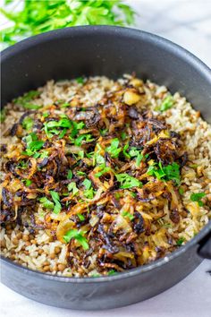 a pan filled with rice and vegetables sitting on top of a white countertop next to a green leafy garnish