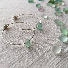 green sea glass beads and silver hoop earrings laying on a white surface with small pieces of sea glass scattered around them