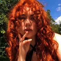 a woman with red hair sitting in the grass and holding her hand to her face