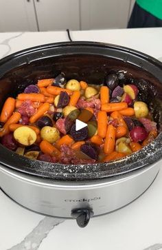 a slow cooker filled with carrots, potatoes and other vegetables sitting on a counter