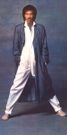 a man in white pants and black coat posing for a photo with his hands on his hips