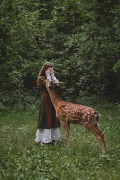 a woman standing in the grass next to a deer with it's head on her hand