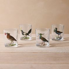 four shot glasses with birds painted on them sitting on top of a wooden table next to each other