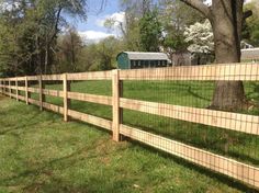 a wooden fence in the middle of a grassy field next to a tree and barn